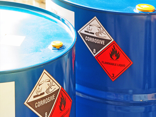 red warning and safety labels adhere to the side of blue metal drums
