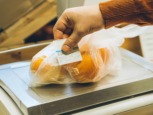 man adhering a linerless label to a plastic bag full of produce in the grocery store