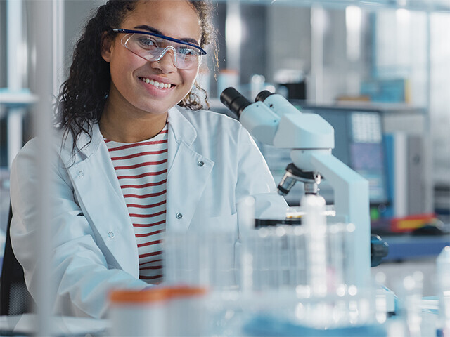 woman behind a microscope smiling