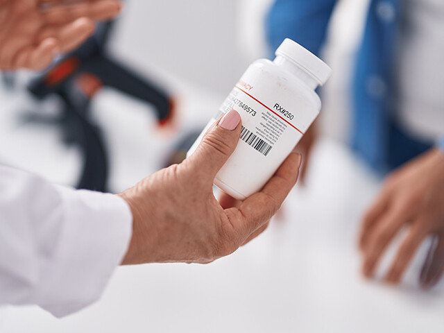 woman in white coat inspecting prescription bottle