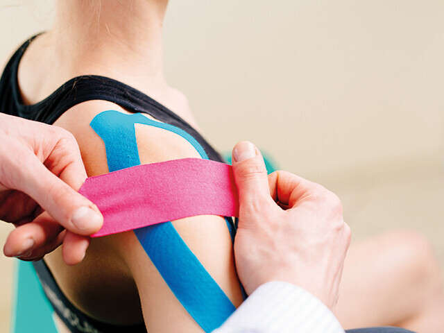 pink and blue medical tape being applied to a shoulder