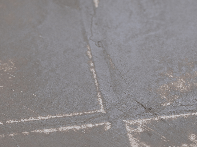 Detail podlahového podkladu s vyplněnými spárami a jemnými trhlinami po aplikaci vyrovnávací hmoty. Povrch je připraven pro další renovaci nebo pokládku podlahové krytiny.