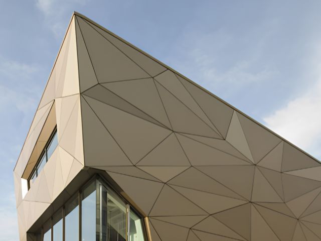 Moderne bygning med geometrisk facadebeklædning i lyse beige nuancer. Facaden har et elegant og ensartet udtryk uden synlige skruer eller mekaniske fastgørelsespunkter.