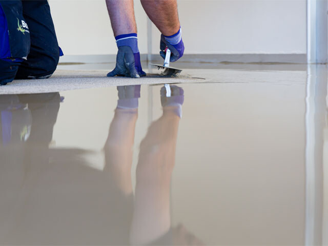 A flooring specialist is applying a layer of self-levelling compound to the substrate