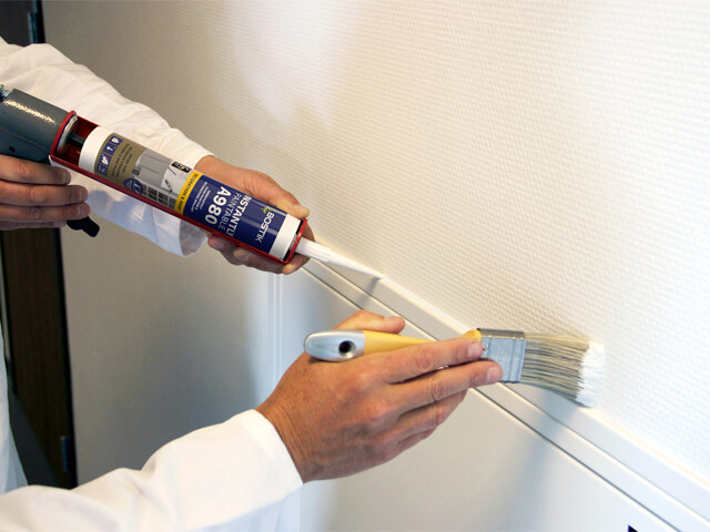 Caulk gun with sealant applying sealant that's followed by a paintbrush