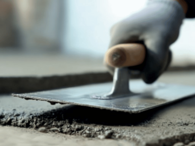 Bostik floor levelling compound being smoothed with a hand trowel over a rough concrete surface to create an even finish.