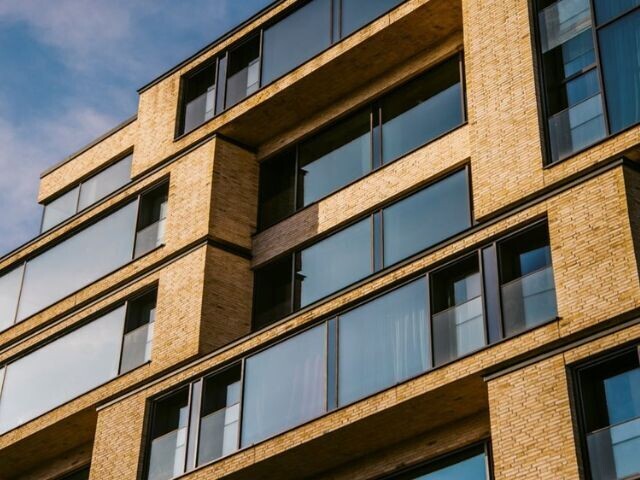 Facade of a building with tall glass windows and tan bricks