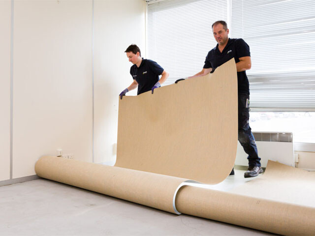 Two guys rolling out a sheet of linoleum to install