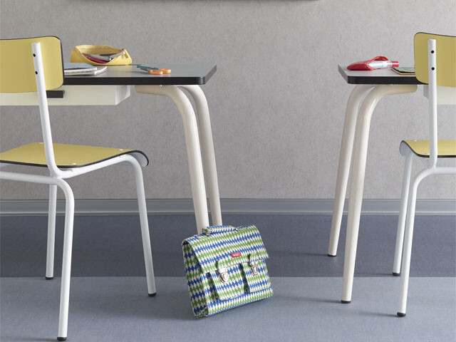 Two chairs in a classroom, with a schoolback leaning against a table leg