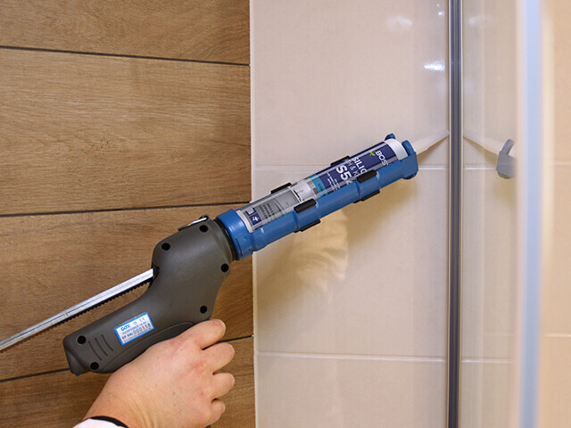 Hand holding a caulkgun to apply sanitary sealant to a shower