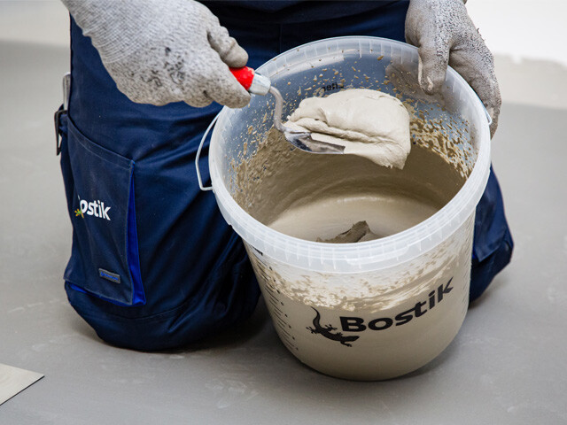 Man kneeling with a clear bucket filled with self-levelling compound