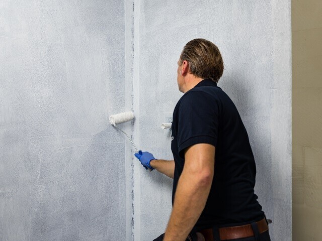 A man applying a liquid waterproofing barrier to a wall