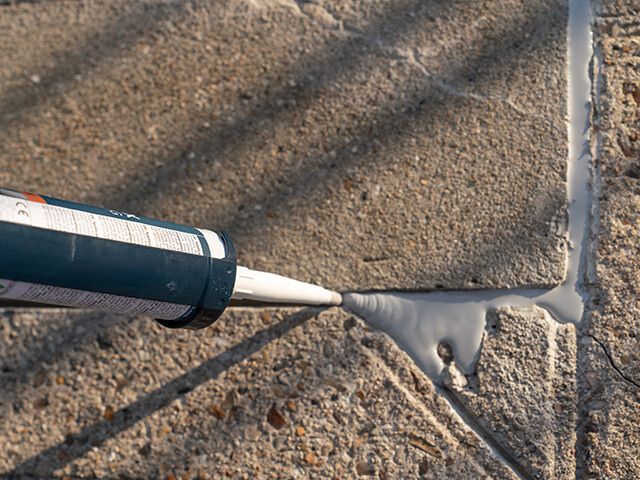 Bostik chemical-resistant sealant being dispensed into a concrete joint, creating a protective seal for outdoor paving applications.
