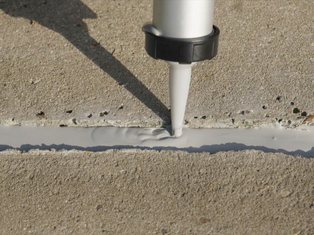 Close-up of Bostik chemical-resistant sealant being applied into a concrete expansion joint, creating a smooth, flexible seal for long-term protection in outdoor paving applications.