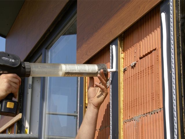 Bostik PanelTack façade cladding adhesive being applied to vertical support profiles during the installation of exterior façade panels on a building.