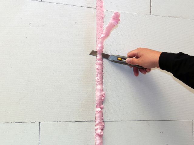 Excess Bostik FP404 Fire Retardant PU Gun Foam being trimmed with a utility knife after curing, creating a neat fire-resistant joint between wall panels.