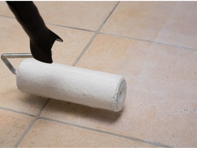 Close-up of a paint roller loaded with Bostik primer positioned on a tiled floor, ready for application.