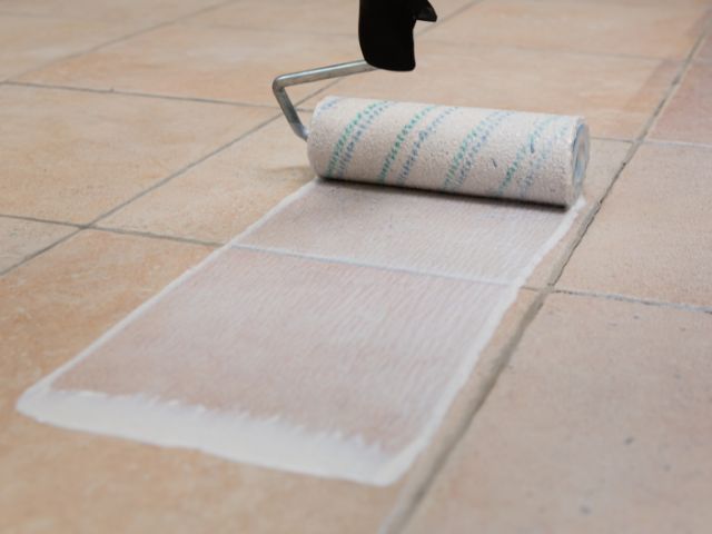 Paint roller spreading a smooth coat of Bostik primer across tile joints, creating an even base for tile installation.