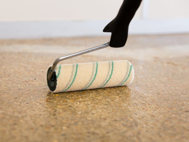 Close-up of a paint roller applying Bostik primer onto a textured floor surface to create a consistent bonding layer.