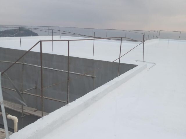 Large flat roof coated with a white waterproofing layer, showing a completed surface treatment using Bostik sealing and protection systems.