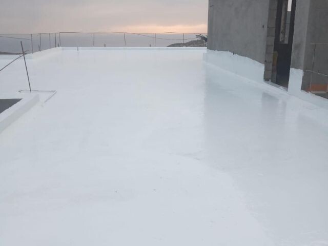 Flat roof coated with a smooth white Bostik waterproofing layer near a building structure, showing freshly applied roof protection.