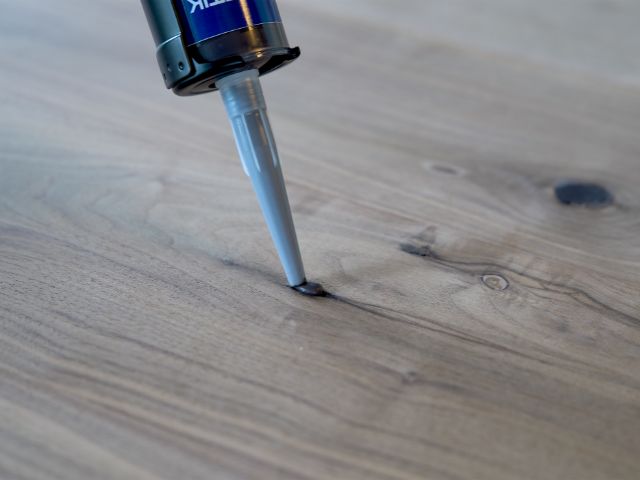 Bostik acrylic sealant being applied into a gap in a wooden floor to fill joints and create a smooth, finished appearance.