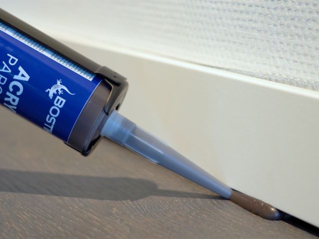 Bostik acrylic sealant being applied along the edge between a skirting board and wooden floor to seal gaps and improve the floor finish.