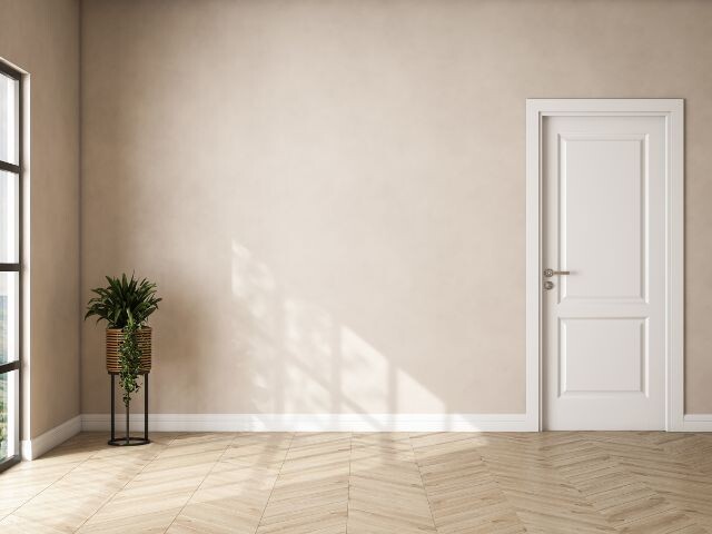 Modern interior with light wood flooring, white skirting boards, a decorative plant and door, showcasing a finished room with sealed flooring and trim details using Bostik products.