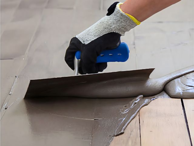 Close‑up of a floor adhesive or levelling compound being spread evenly with a wide smoothing trowel.