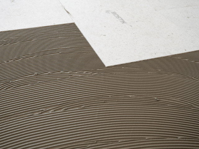 Close-up of evenly combed Bostik adhesive on a subfloor surface, ready for placement of flooring panels.