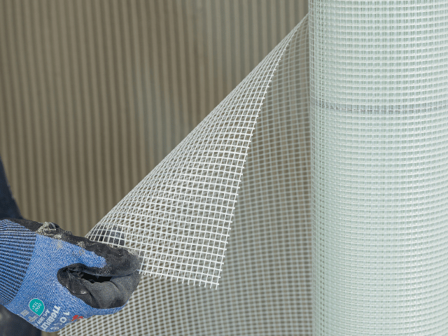 Close-up of Bostik reinforcement mesh being unrolled and positioned over an adhesive-coated surface for floor preparation.