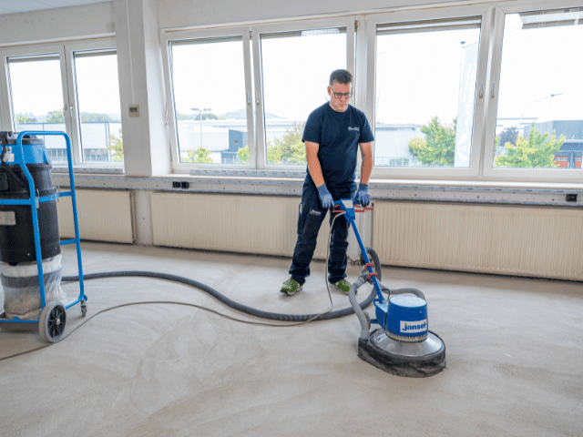 Floor surface being sanded with a polishing machine connected to a vacuum system during Bostik floor preparation process.