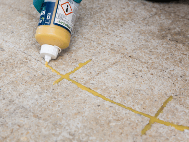 Bostik RENO repair resin being applied from a squeeze bottle into cracks on a concrete floor for precise sealing and reinforcement.