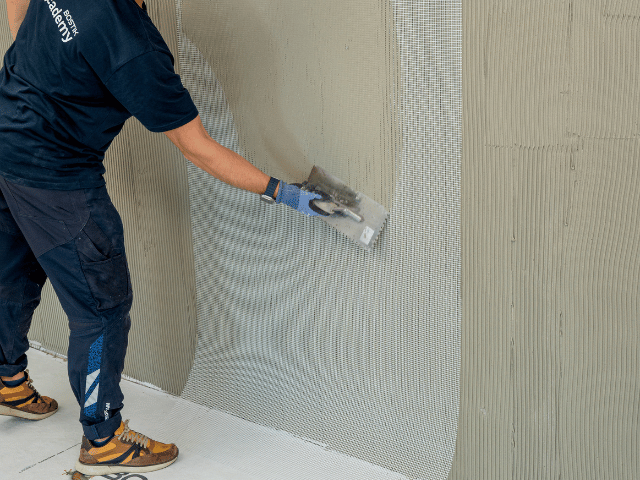 Bostik reinforcement mesh being applied onto a wall with a trowel to embed it into a fresh layer of adhesive or levelling compound.