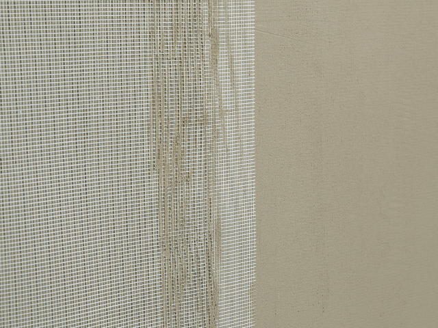 Close-up of Bostik reinforcement mesh partially embedded in a levelling compound layer on a wall surface.