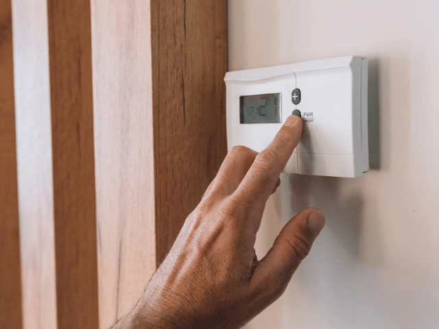 Hand adjusting a wall-mounted thermostat after completing flooring installation using Bostik renovation system.