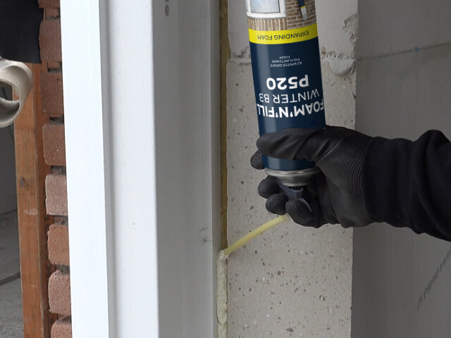 Main appliquant de la mousse expansive à l’aide d’une bombe Bostik dans l’espace entre un cadre de fenêtre et un mur en maçonnerie pour l’isolation et l’étanchéité