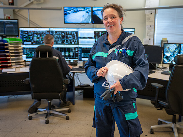 female arekma employee in workwear holding hard hat stood in control room