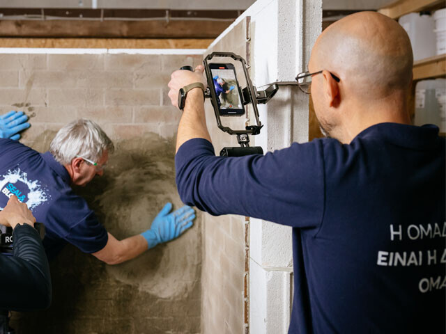 Two guys recording a thrid who's applying grout to waterpro