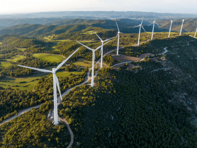 Doğal peyzaj üzerinde konumlanan rüzgar türbinleri, daha düşük CO₂ emisyonları ve sürdürülebilir yapı çözümlerini temsil eder.