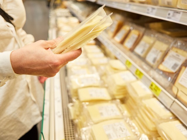 person holds a pre-packaged piece of cheese in a grocery store