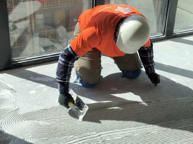 Closeup of man applying adhesive to flooring.