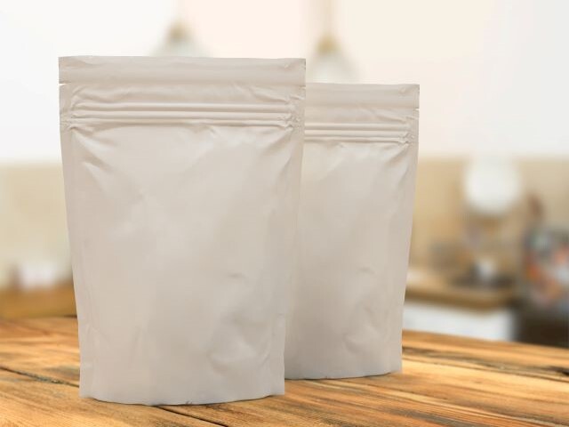 Blank white half pound pouches stand erect on a wooden countertop, waiting to be finished with Bostik's PUREKOTE coatings.