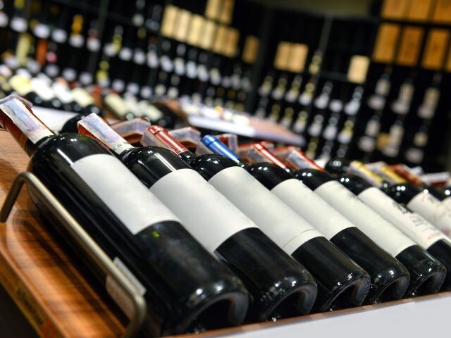 A row of red wines sit on display at a 45 degree angle with their labels facing upwards.