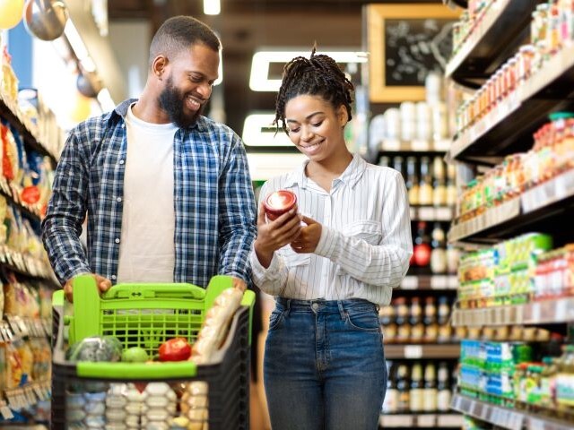 A couple grocery shopping together, review a package in the middle of an aisle.
