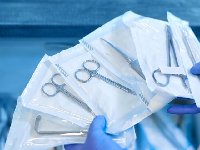 A gloved medical professional handles multiple prepacked sterile scissors in preparation for surgery.