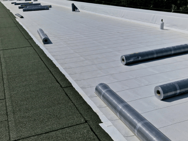 Flat roof surface with roofing membrane laid out and several membrane rolls positioned for installation.