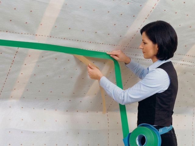 Woman applying black seaming tape along the edge of a roof insulation panel during installation.