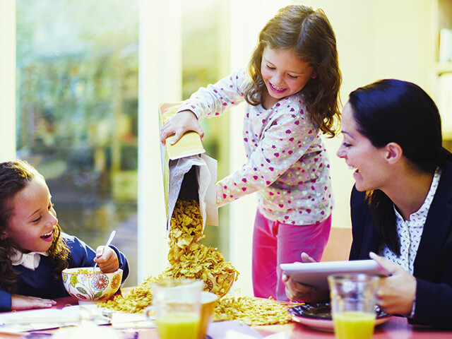 young girl pouring cereal into a bowl at a breakfast table